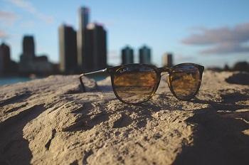 Pair of sunglasses sitting on a rock with a city skyline in the background