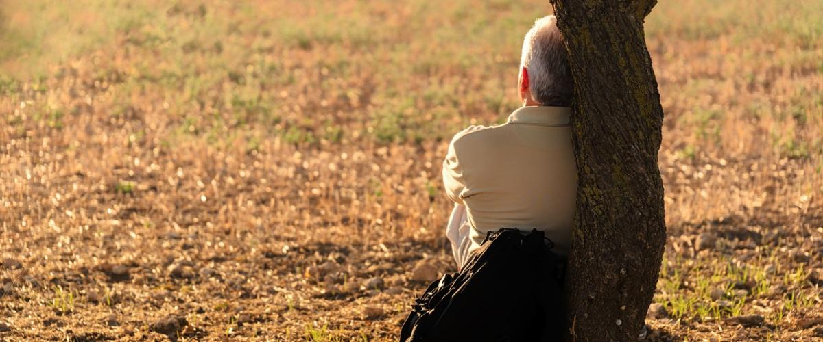 Man with backpack sitting against a tree