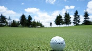 Golf ball sitting on grass with a person in the background